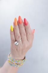 Multicolored manicure, female hands with colored nails, nail polishes, yellow, orange and pink colors.