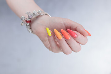 Multicolored manicure, female hands with colored nails, nail polishes, yellow, orange and pink colors.