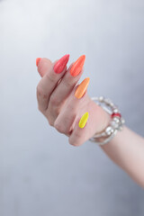 Multicolored manicure, female hands with colored nails, nail polishes, yellow, orange and pink colors.