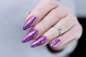 Woman hand with long nails and a bottle of plum purple nail polish