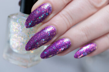 Woman hand with long nails and a bottle of plum purple nail polish