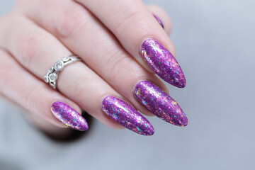 Woman hand with long nails and a bottle of plum purple nail polish