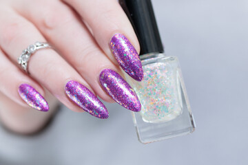 Woman hand with long nails and a bottle of plum purple nail polish