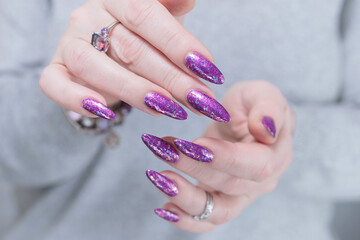 Woman hand with long nails and a bottle of plum purple nail polish