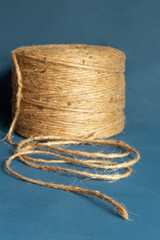 Close-up of a tightly coiled natural twine roll spool against a blue background, with the frayed start in sharp focus, showcasing the texture and fibers of the twine for a natural and sustainable look