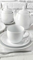 Fototapeta premium A set of white porcelain dinnerware, including plates, cups, saucers, a teapot, and a sugar bowl, arranged on a white table in front of a white brick wall