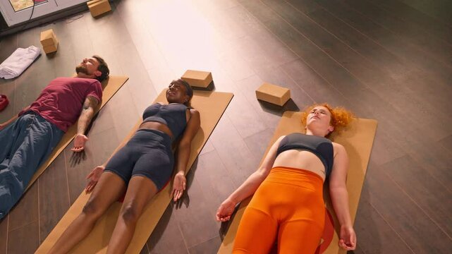 A two woman and a man lying on a yoga mat in a relaxed position, possibly meditating or resting after a workout. 