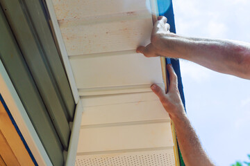 Installing vinyl soffit plastic panels on facade ceiling of new home by an employee