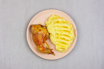 fried chicken leg and mashed potatoes in a pink plate on a gray table top view