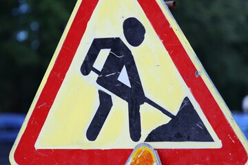A man holds a shovel near a yellow and red sign on a construction site.