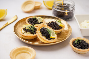 Plate of tasty tartlets with black caviar on grey background
