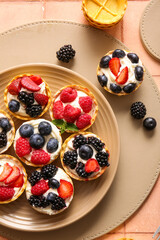Plate of tasty tartlets with whipped cream and berries on pink tile background