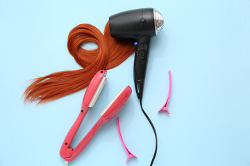 Hair dryer, strand, flattening iron and clips on light blue background