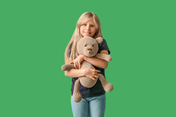 Cute little girl with plush teddy bear on green background