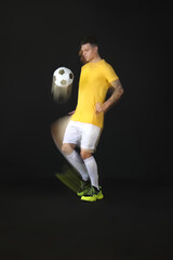 Young man playing with soccer ball in motion on black background