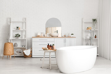 Table with skin care products near white bathtub in light bathroom