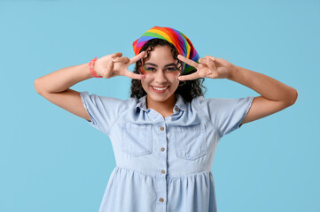 Young African-American woman with rainbow headscarf showing victory gesture on blue background. LGBT concept
