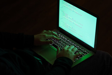 Hacker using laptop in dark room, closeup
