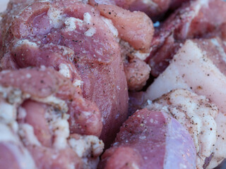 A closeup shot of raw meat cut into pieces, marinated with salt and pepper.