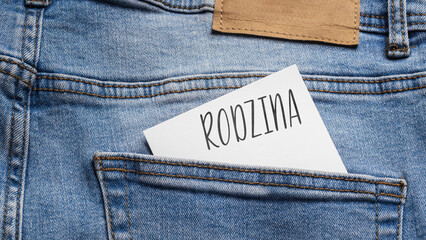 White card with a handwritten inscription "Rodzina", inserted into the pocket of blue pants jeasnow (selective focus), translation: Family
