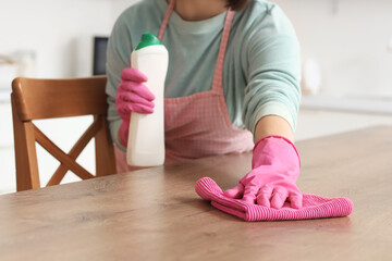 Woman cleaning wooden table with rag in kitchen, closeup