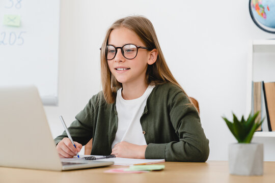 Smart caucasian schoolgirl student pupil learning online, using laptop, listening to lessons from home, doing homework on lockdown