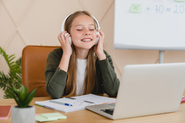 Happy child caucasian student pupil schoolgirl studying remotely, doing homework for school, using...