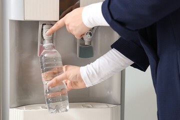 Woman filling plastic bottle with filtered water from cooler in office