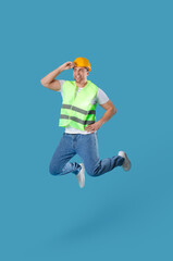 Young male builder jumping on blue background