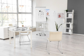 Fototapeta premium Blurred view of oculist's office with workplace and eye test charts