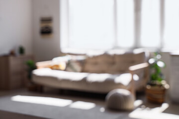 Blurred view of light living room with sofa and window
