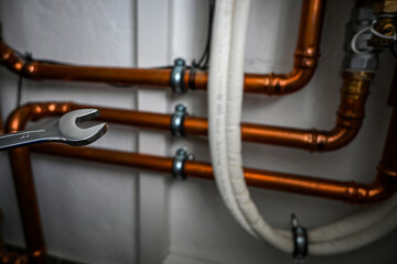 Obraz premium Plumber is holding a wrench and repairing copper water pipes in a boiler room