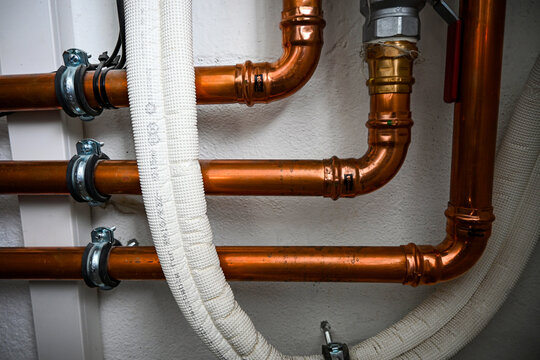 Copper water pipes are being fixed to a wall by a plumber during the installation of a heating system