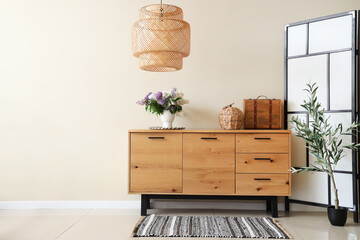 Vase with lilacs on wooden chest of drawers and lamp in stylish room