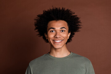 Portrait photo of young funky toothy smile guy with curly haircut wearing gray t shirt optimist isolated on brown color background