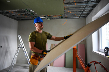 Construction worker carrying a large plasterboard with the help of a drywall lift, on a construction site