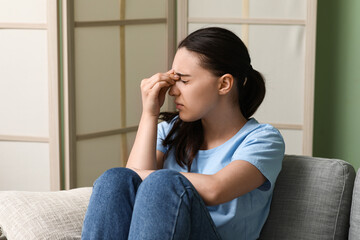 Young woman suffering from headache and sitting on sofa at home