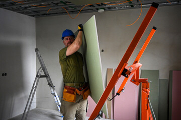 Construction worker carrying a large plasterboard with the help of a drywall lift, on a construction site