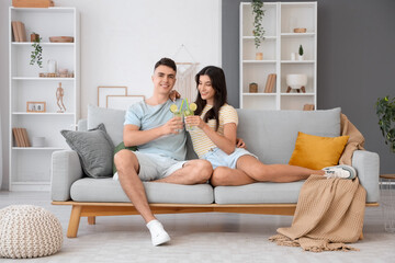 Happy young couple with glasses of mojito sitting on sofa at home