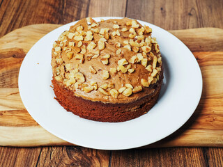 A dessert cake in brown color with nuts in a plastic container on a wooden table. Bakery product, party food. Tasty snack.