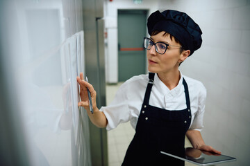 Female chef going through order list while using touchpad in  kitchen.