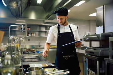 Male chef taking notes while going through food supplies in  kitchen.