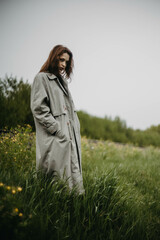 beautiful woman in a gray coat posing in nature in cloudy weather, gloomy mood.