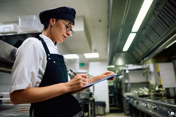 Female cook taking notes while creating  menu in restaurant.