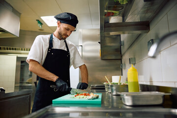 Restaurant cook chopping food while preparing meal in  kitchen.