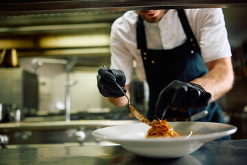 Close up of professional cook serving pasta in restaurant.
