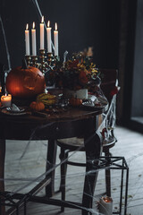 Beautiful table with homemade delicious cake for Halloween party with meringue ghosts and chocolate pumpkins. Candles in chandelier, spider web, jack-o-lantern for festive holiday decoration. Dark