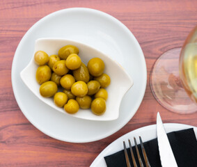 Savory pickled green olives served in white bowl with glass of light wine for relaxing dinner. Traditional Spanish appetizer