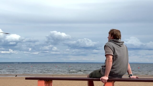 Young man sitting on a bench on beach and enjoying sea view