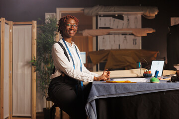 Portrait of happy african american seamstress entrepreneur working in black owned atelier shop...